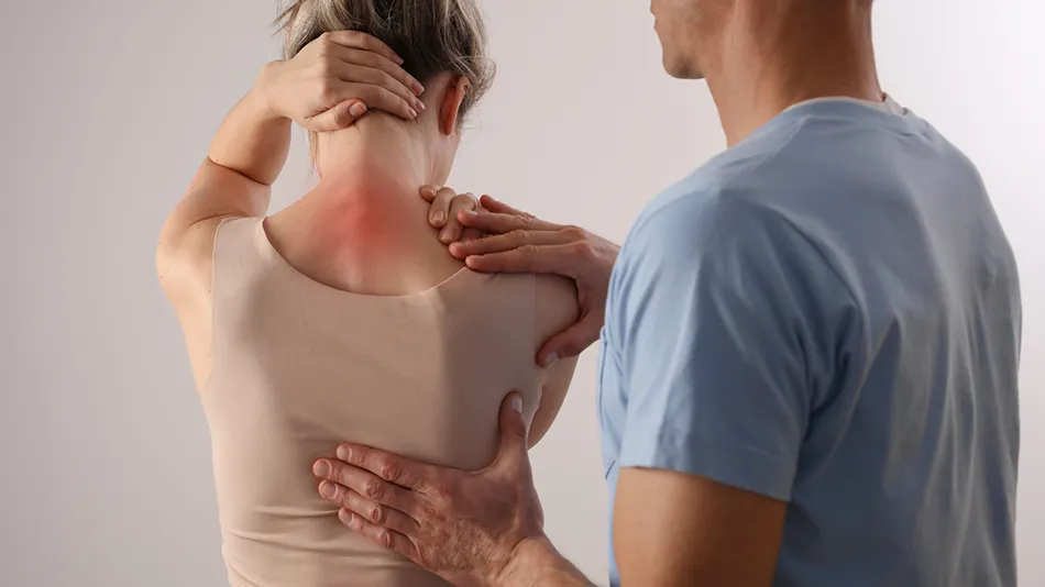 Practitioner examining a woman's upper back and shoulder blade while she holds the back of her neck, with redness highlighting pain at the base of the neck